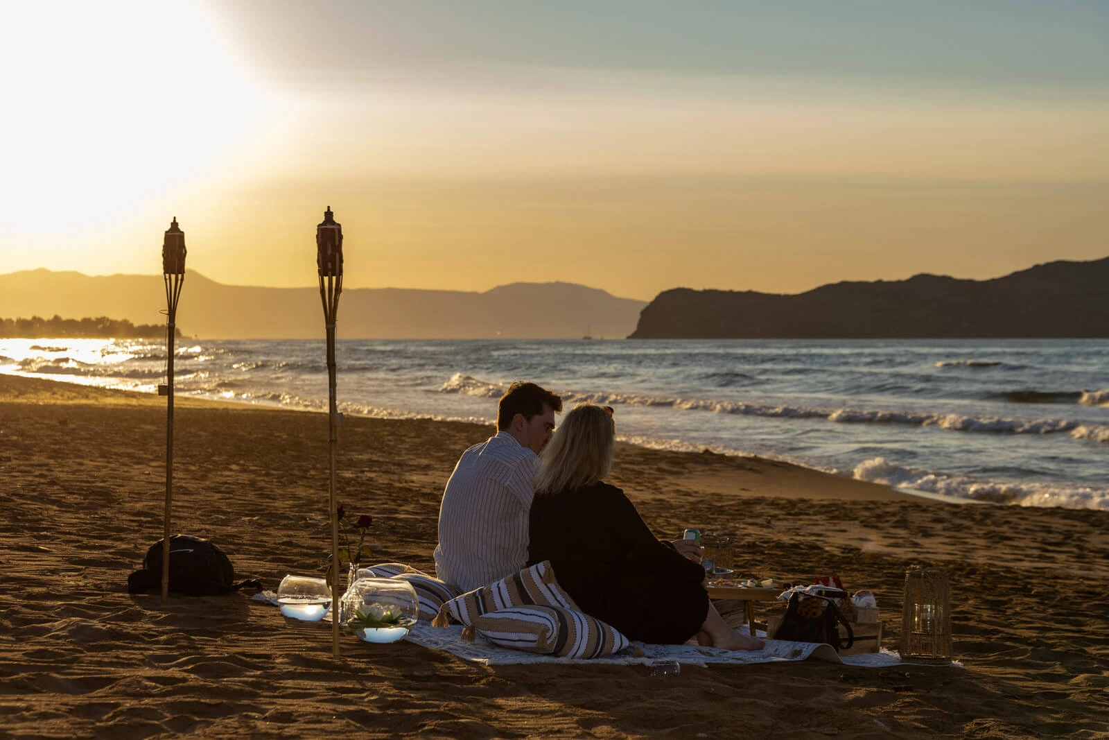 Romantic beach proposal setup at sunset in Crete with couple sitting by the sea
